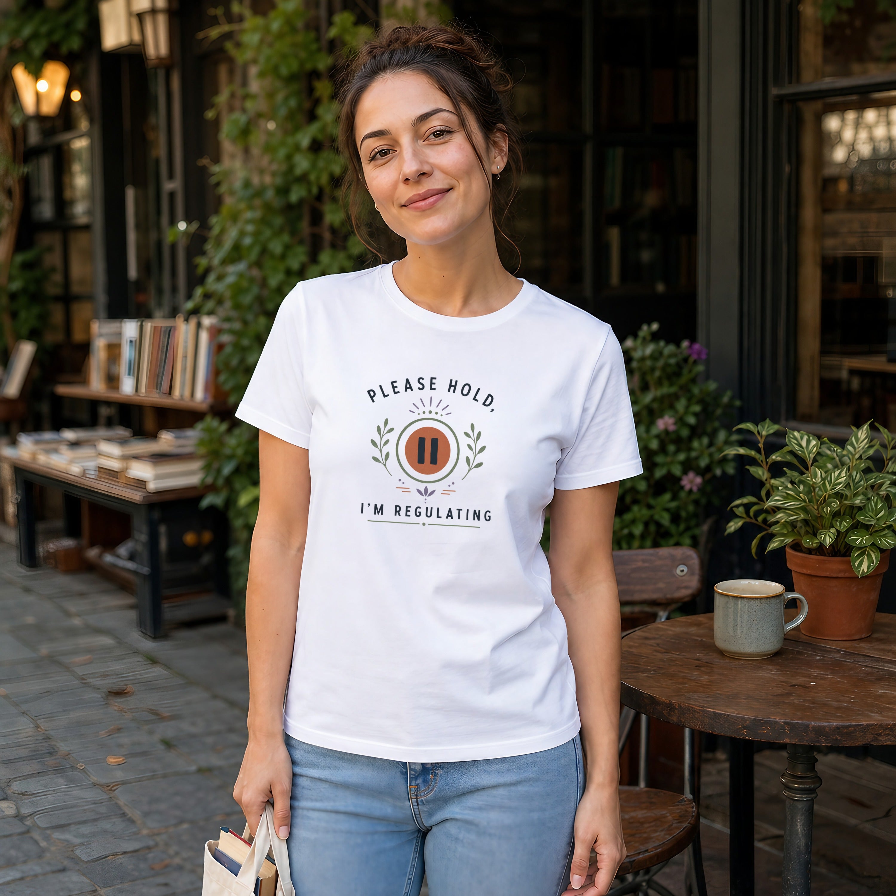 White t-shirt with "PLEASE HOLD, I'M REGULATING" text and a pause symbol.