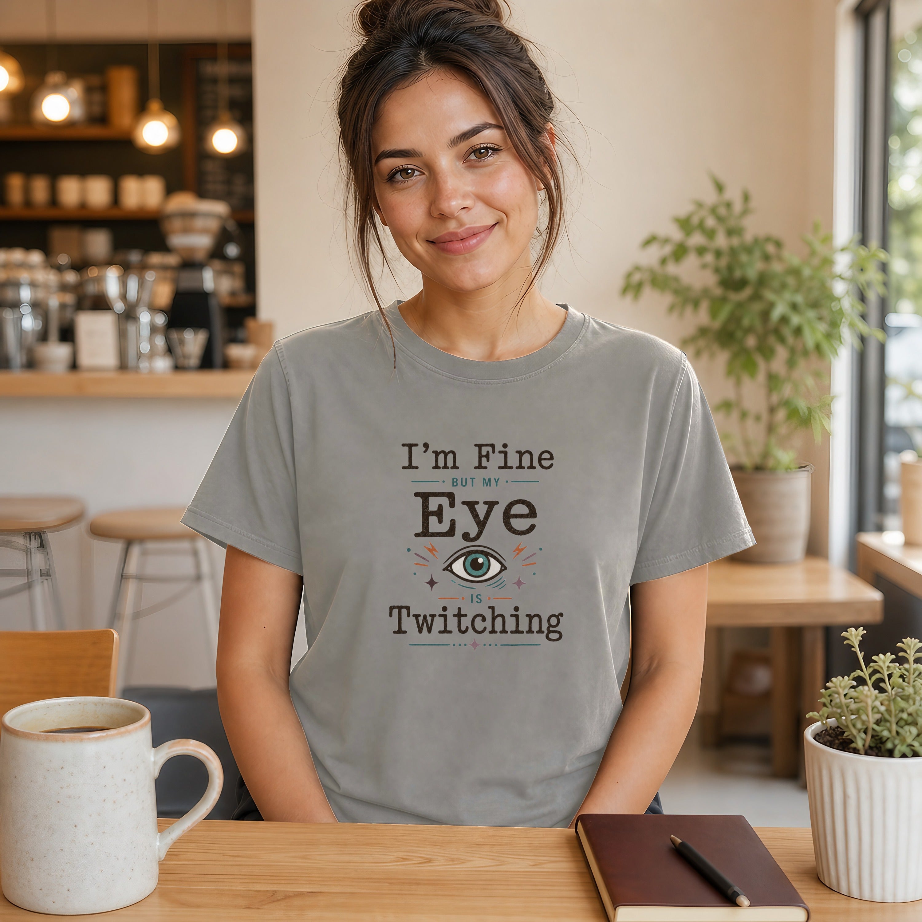 Woman wearing a grey t-shirt that says "I'm Fine but my Eye is Twitching".