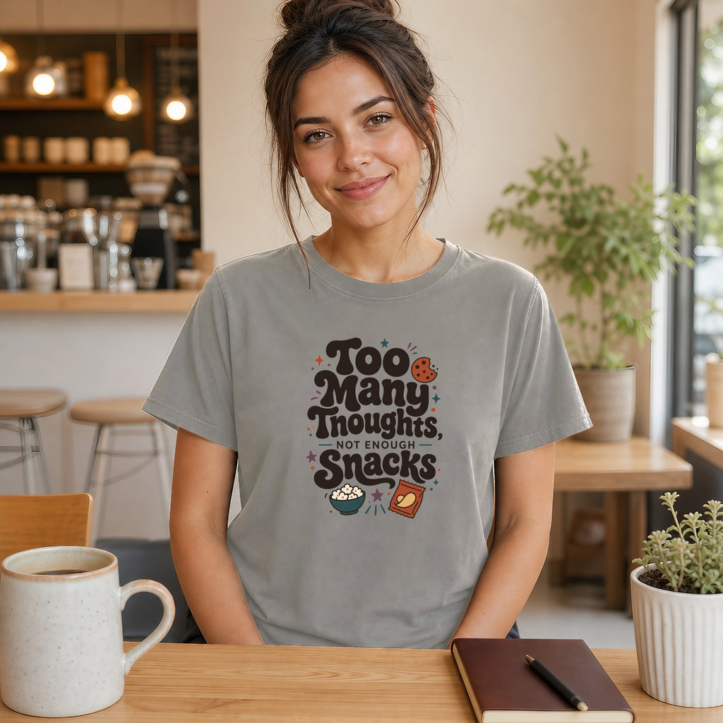 Woman wearing a gray t-shirt with "Too Many Thoughts, Not Enough Snacks" text and snack graphics.