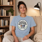 Light blue t-shirt with "Tiny Social Battery Club" logo featuring a battery icon.