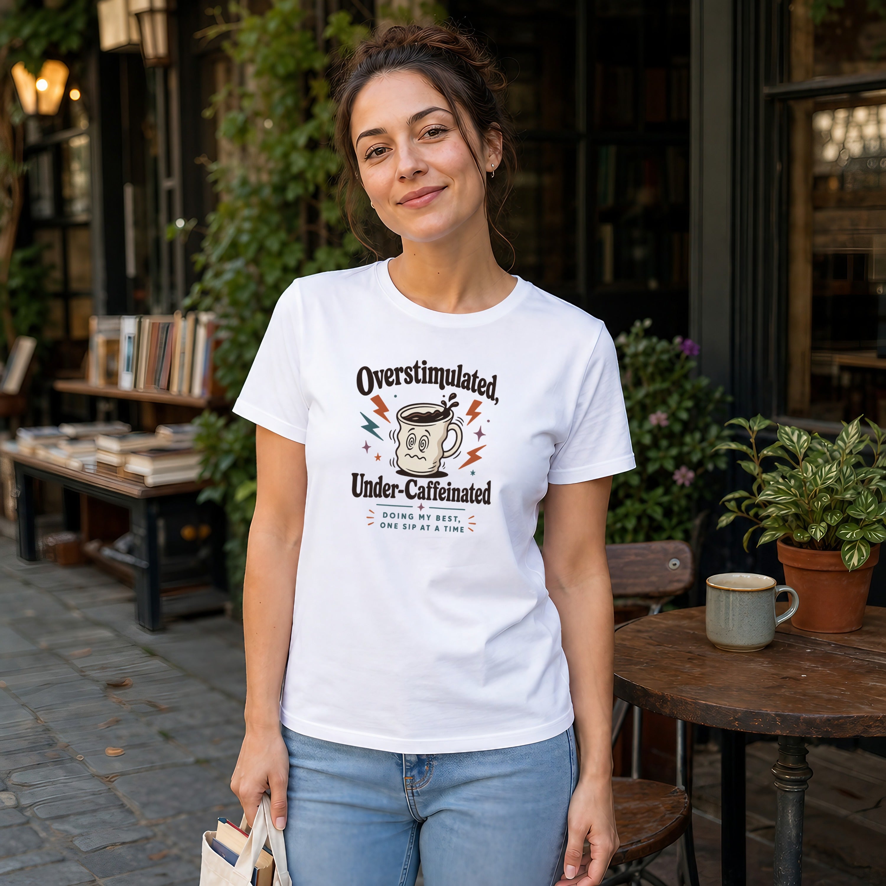 Woman wearing white t-shirt with "Overstimulated, Under-Caffeinated" text design.