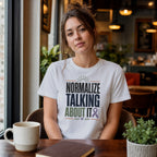 Woman in white t-shirt with text "Normalize Talking About It" and purple ribbon graphic.