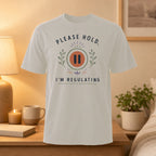 White t-shirt with "Please Hold, I'm Regulating" text and pause symbol.