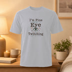 White t-shirt with text "I'm Fine But My Eye Is Twitching" and an eye graphic.