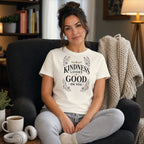 Woman in t-shirt with floral "Kindness Looks Good On You" text, sitting in armchair.