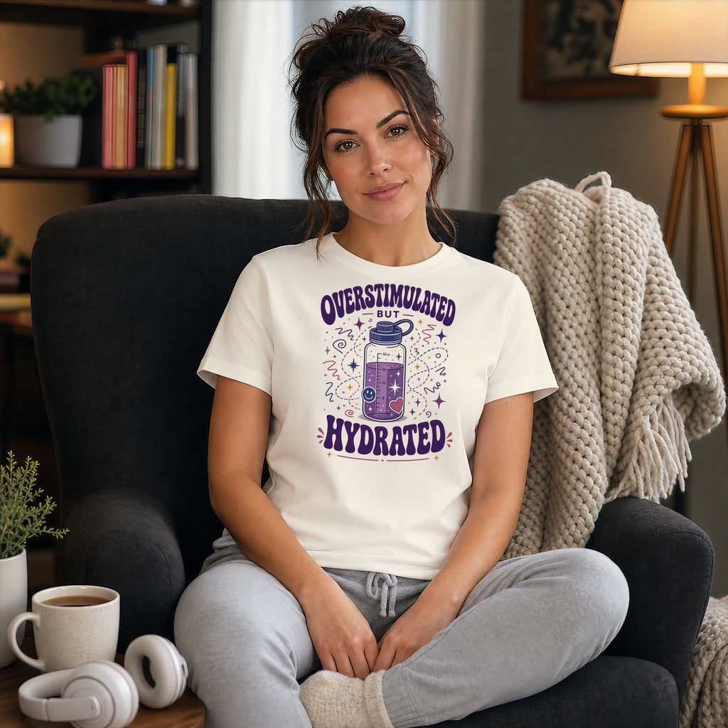 Woman in t-shirt with "Overstimulated but Hydrated" graphic sitting in armchair.