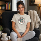 Woman wearing cream t-shirt with "Overthinking Club" logo sitting in armchair.