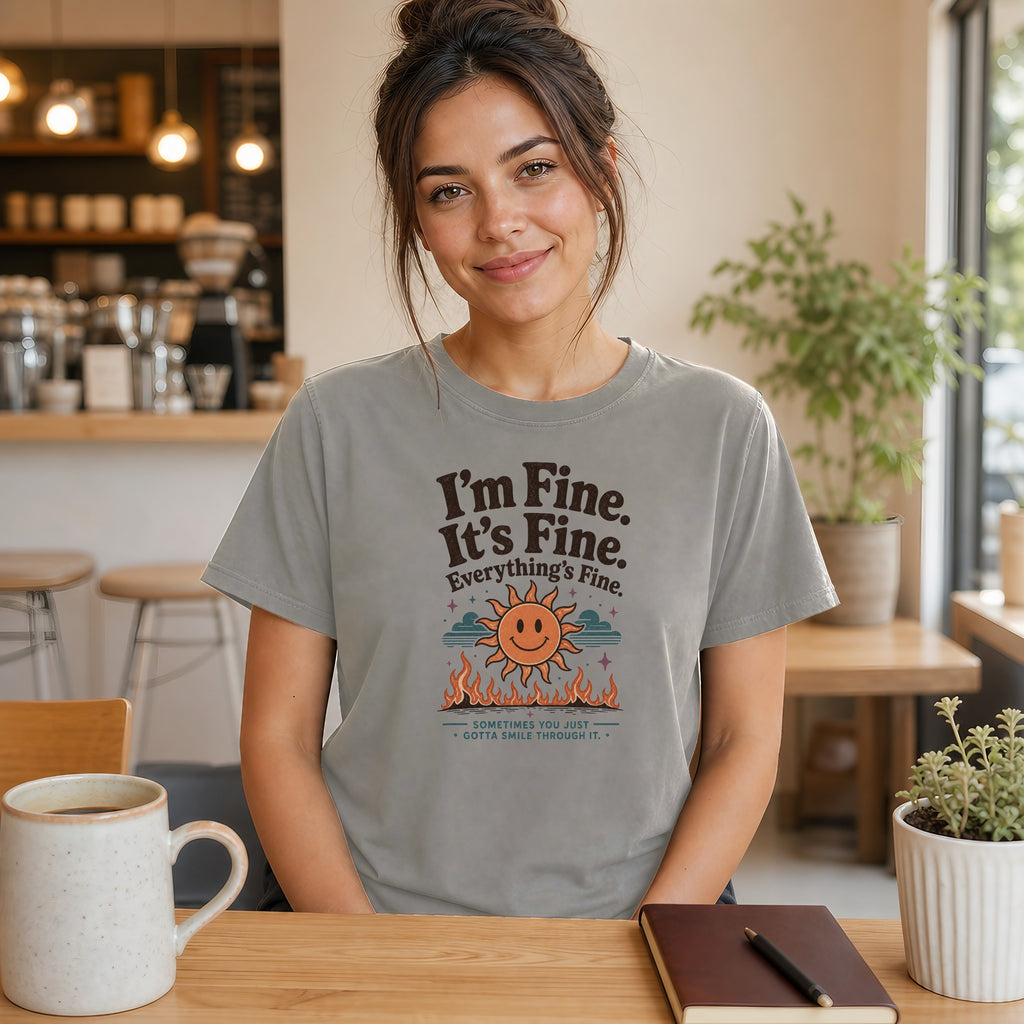 Woman wearing gray t-shirt with "I'm Fine. It's Fine. Everything's Fine." text and smiling sun.