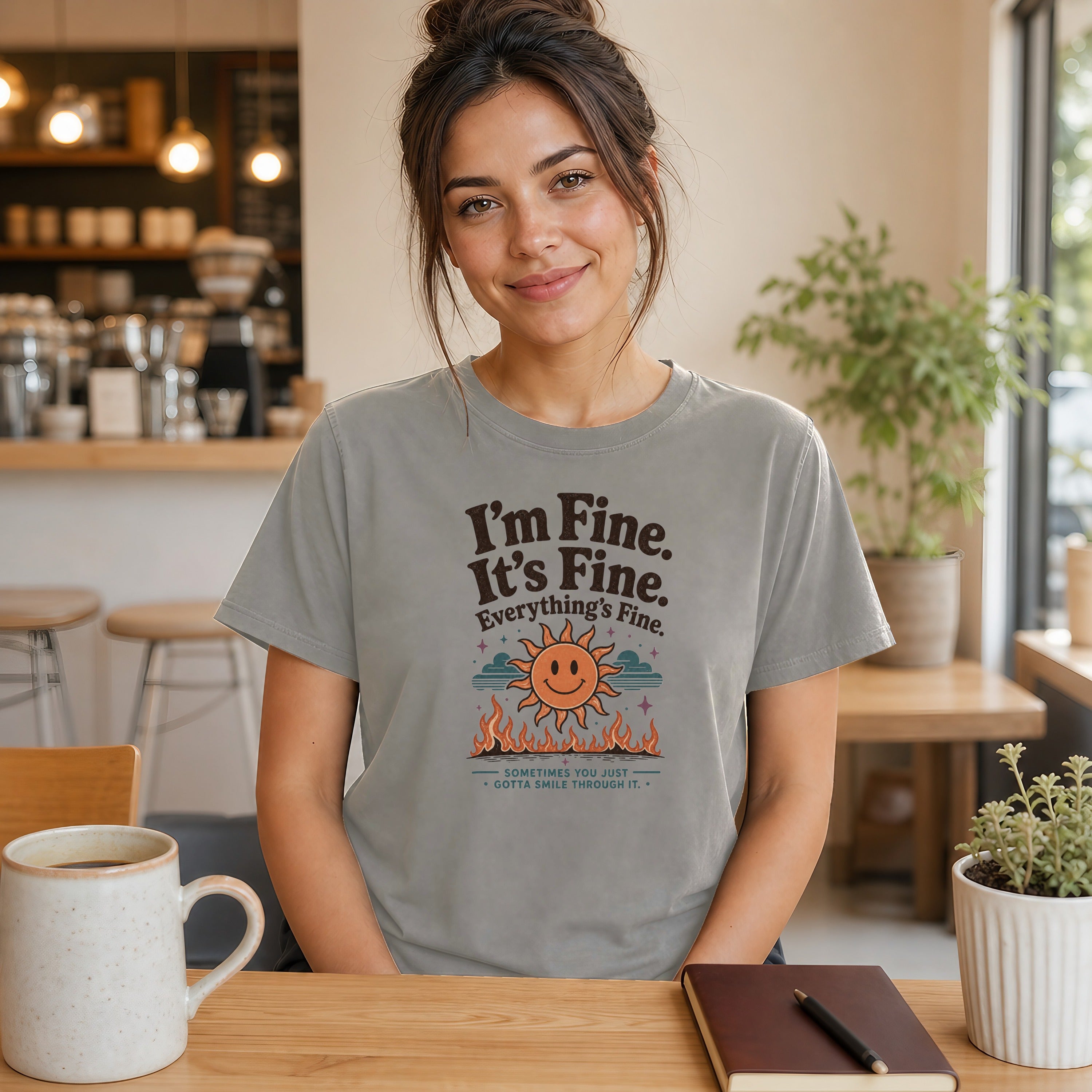 Woman wearing gray t-shirt with "I'm Fine. It's Fine. Everything's Fine." text and smiling sun.