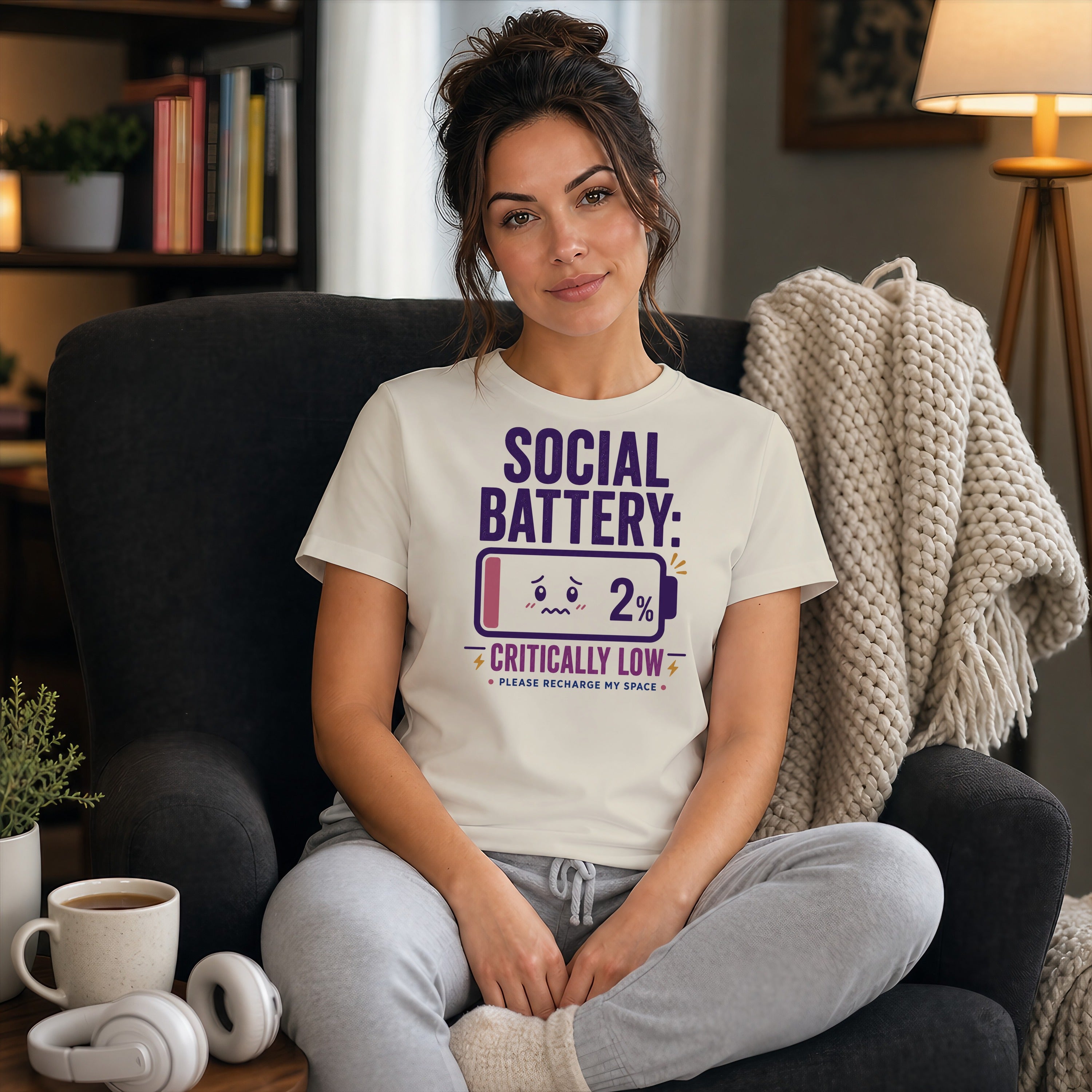 Woman wearing a "Social Battery: Critically Low 2%" t-shirt with headphones nearby.