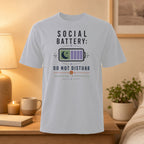 White t-shirt with "SOCIAL BATTERY: DO NOT DISTURB CHARGING IN PROGRESS" text and battery icon.
