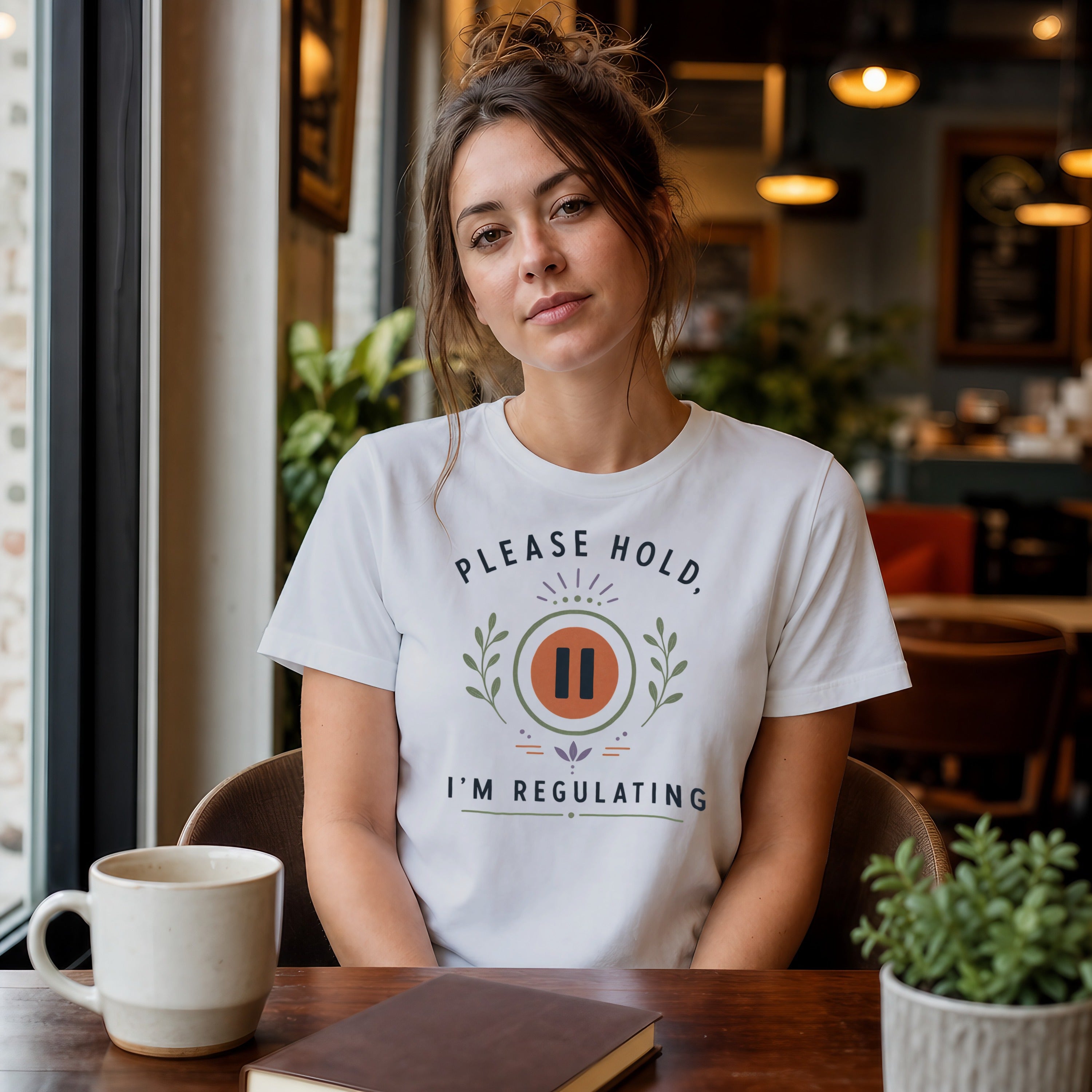 Woman wearing a white t-shirt with "Please Hold, I'm Regulating" text and paused icon.