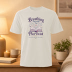 White t-shirt with "Breathing Through the Plot Twist" text and open book graphic.