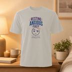 White t-shirt with "Resting Anxious Face" graphic and cartoon emoji.
