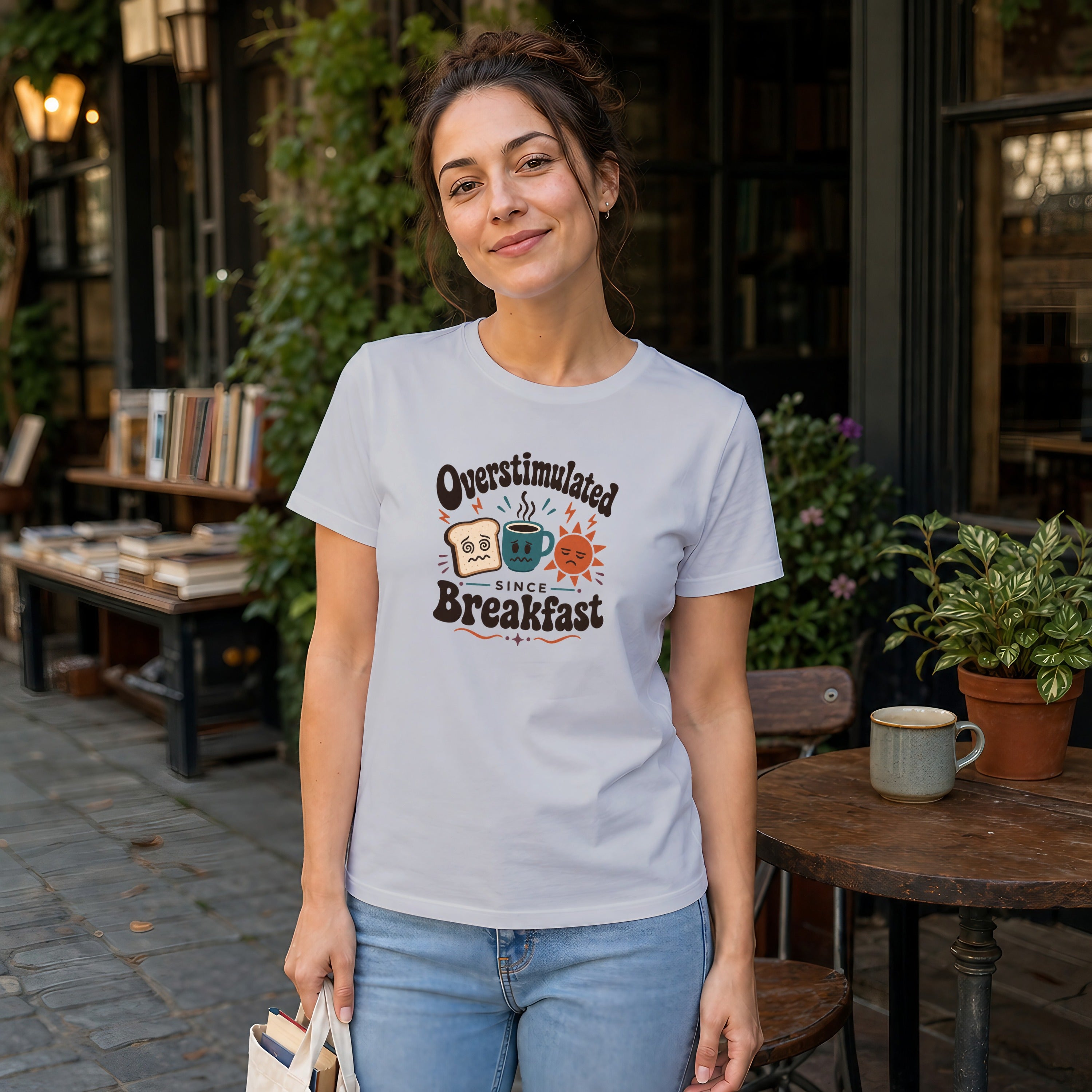 Woman wearing a white t-shirt with "Overstimulated Since Breakfast" text and graphic.