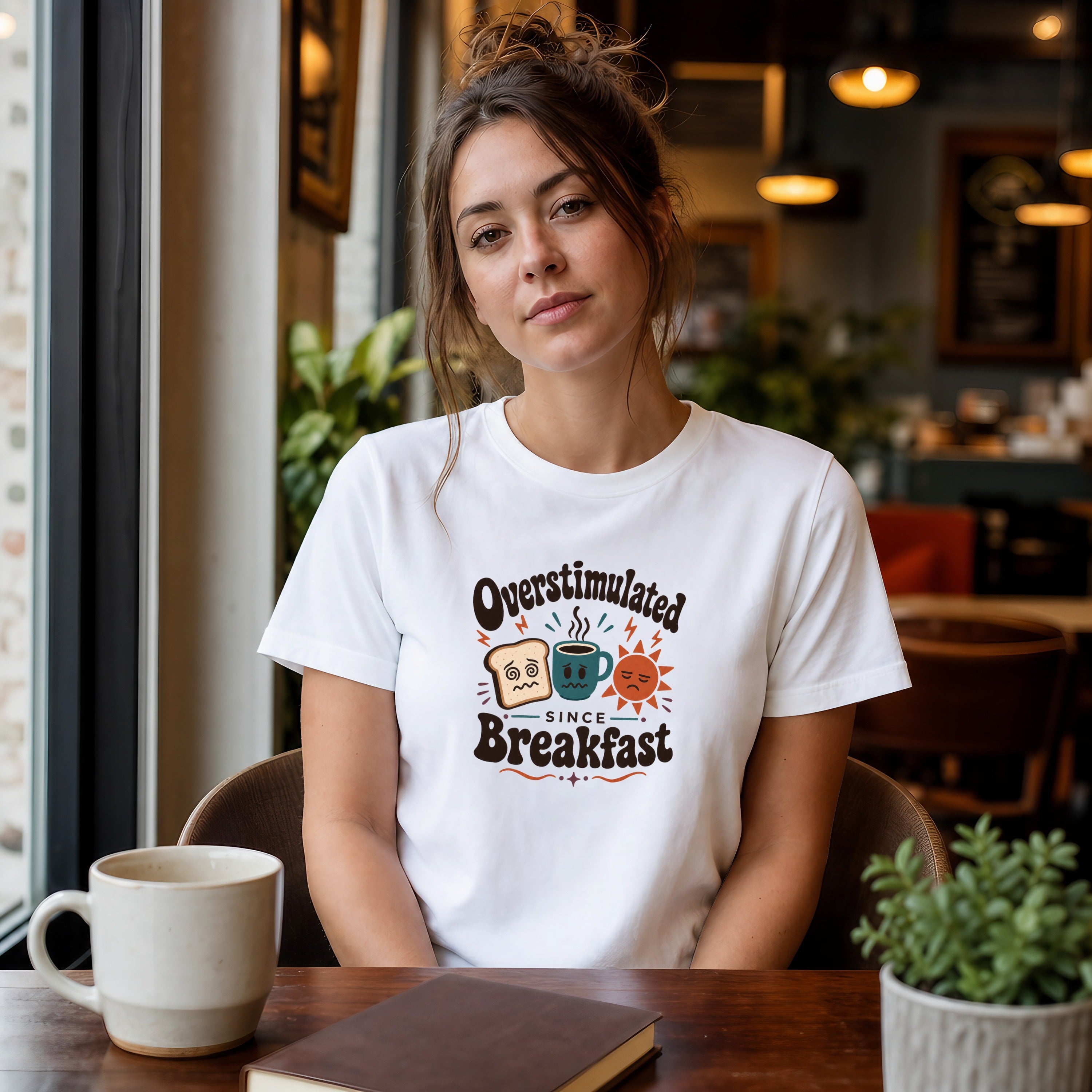 Woman wearing a white t-shirt with "Overstimulated Since Breakfast" graphic.