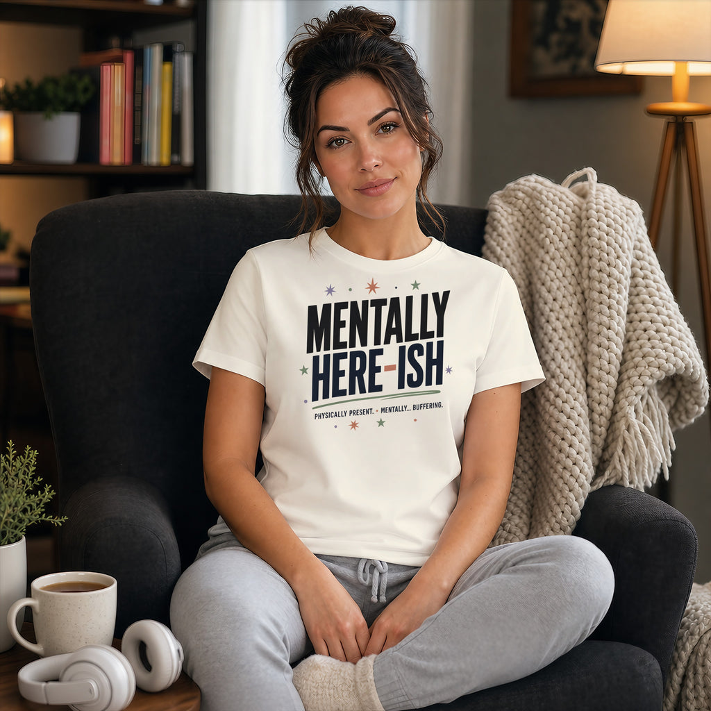 Woman in cream t-shirt with "MENTALLY HERE ISH" text, sitting in chair.