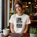 Woman wearing cream t-shirt with "Low Battery, High Standards" text.