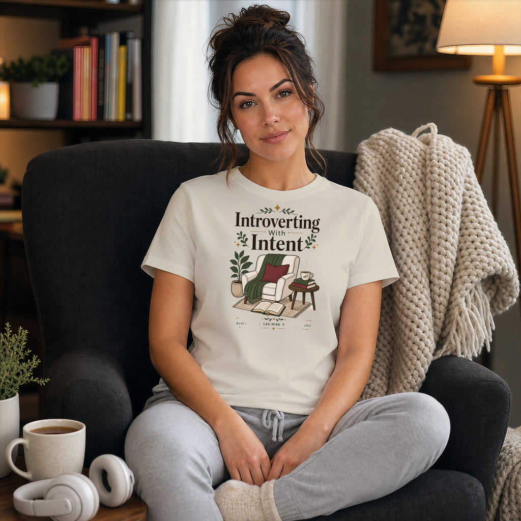 Woman wearing "Introvert With Intent" t-shirt, sitting in armchair with book.