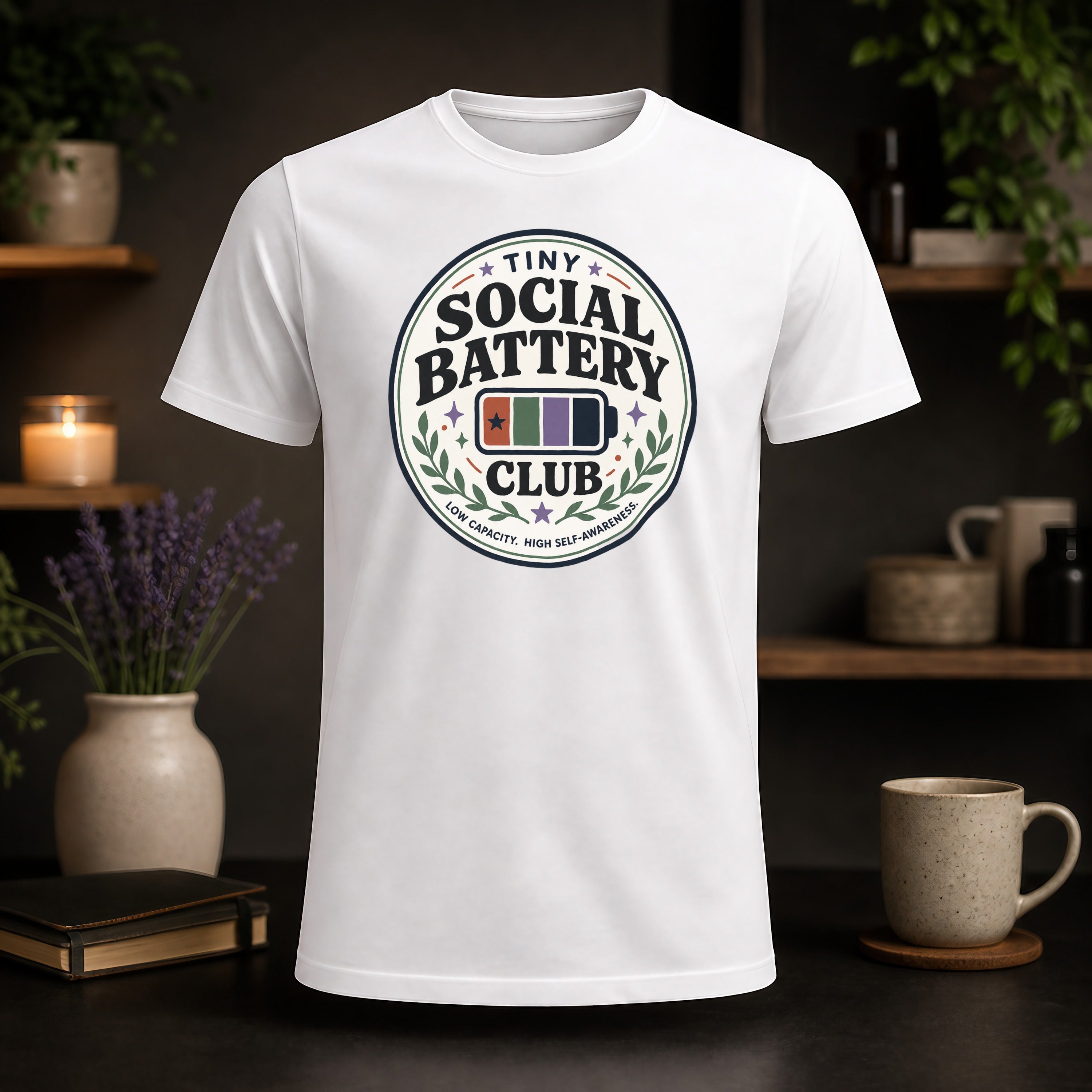 White t-shirt with "Tiny Social Battery" logo and "Low Capacity, High Self-Awareness" text.