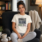 Woman in armchair wearing t-shirt with "Normalize Talking About It" text.